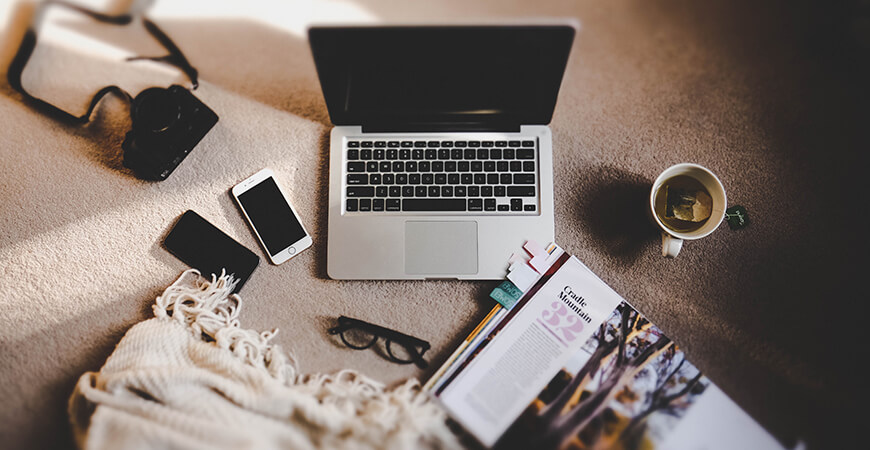 A laptop and phone on the floor next to some magazines