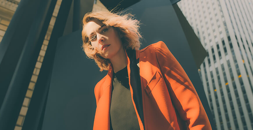 A woman in an orange jacket standing next to a wall.